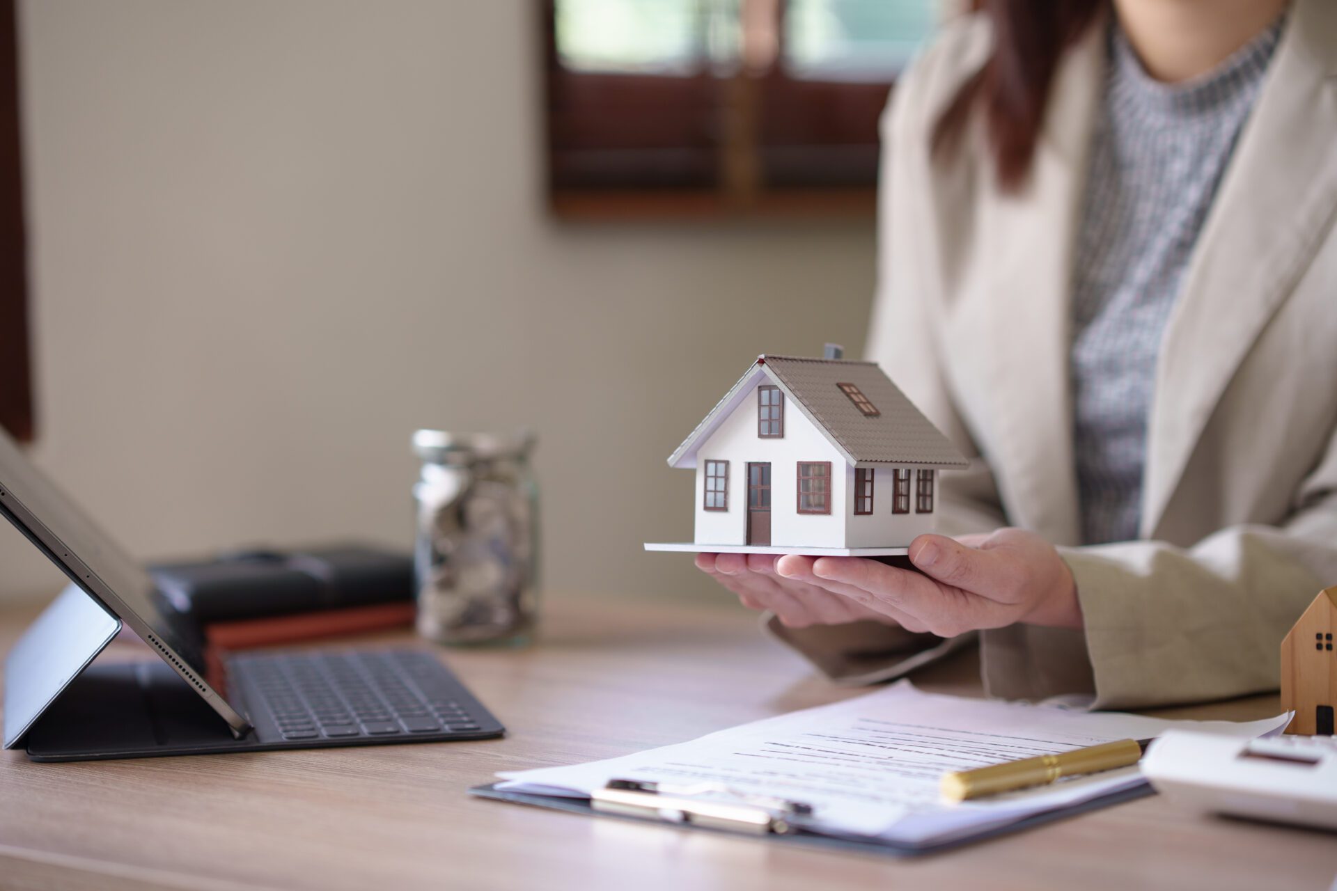 Person holding miniature house at desk.