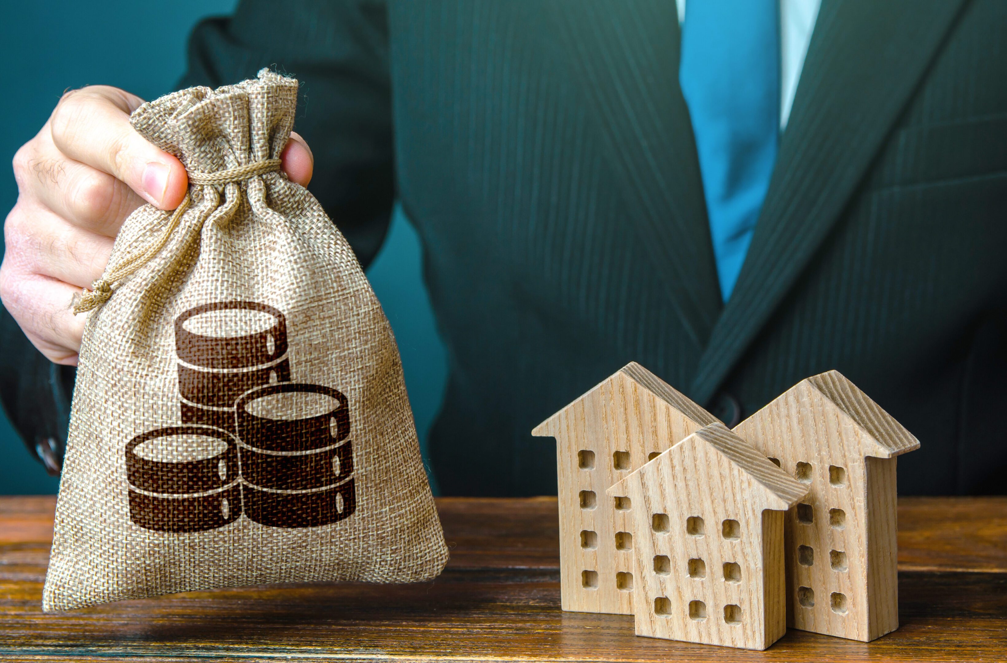 Money bag in a hand and residential buildings figures. Investments in real estate and construction industry. Bank offer of mortgage loan. Rental business. Sale of housing. Buy. Municipal budget. Taxes
